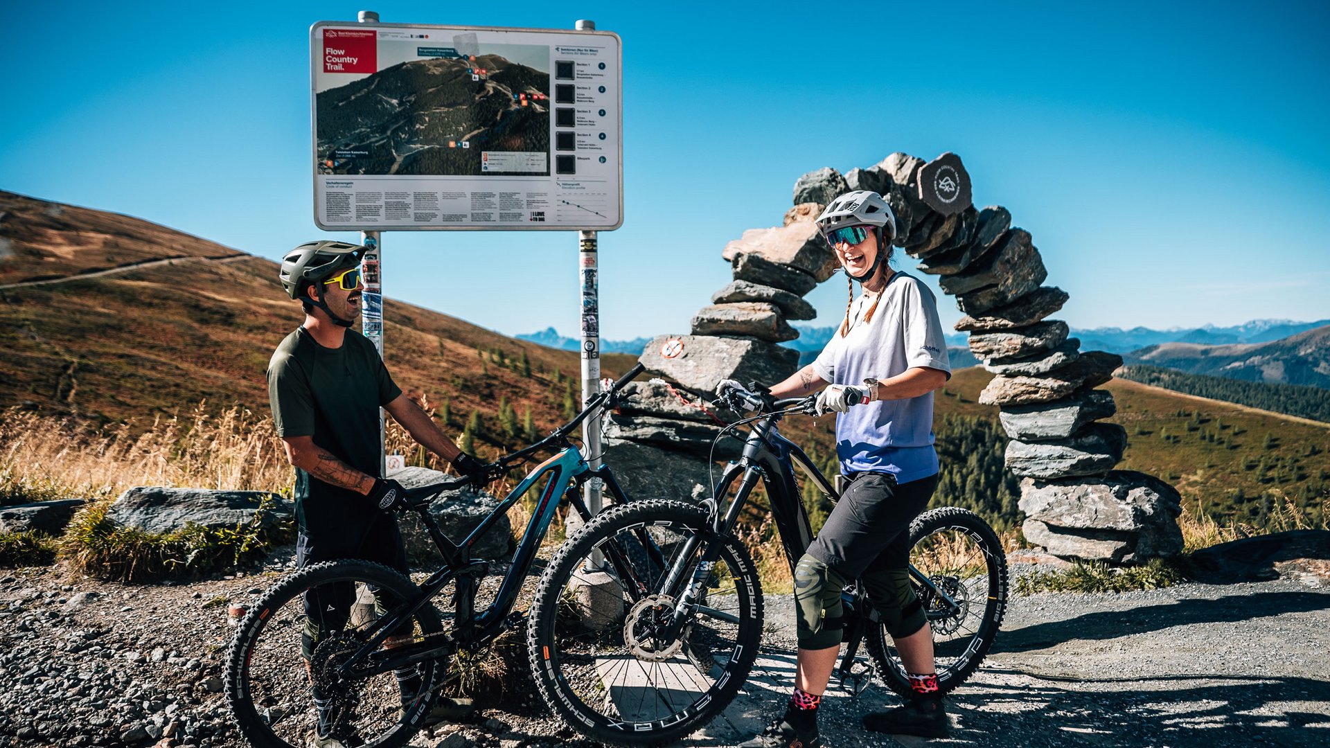 Zwei Mountainbiker mit Helmen an einer Wegbeschreibung in den Bergen (© Jens Scheibe)