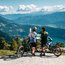 Zwei Mountainbiker lesen eine Tafel mit Berg- und Seeblick