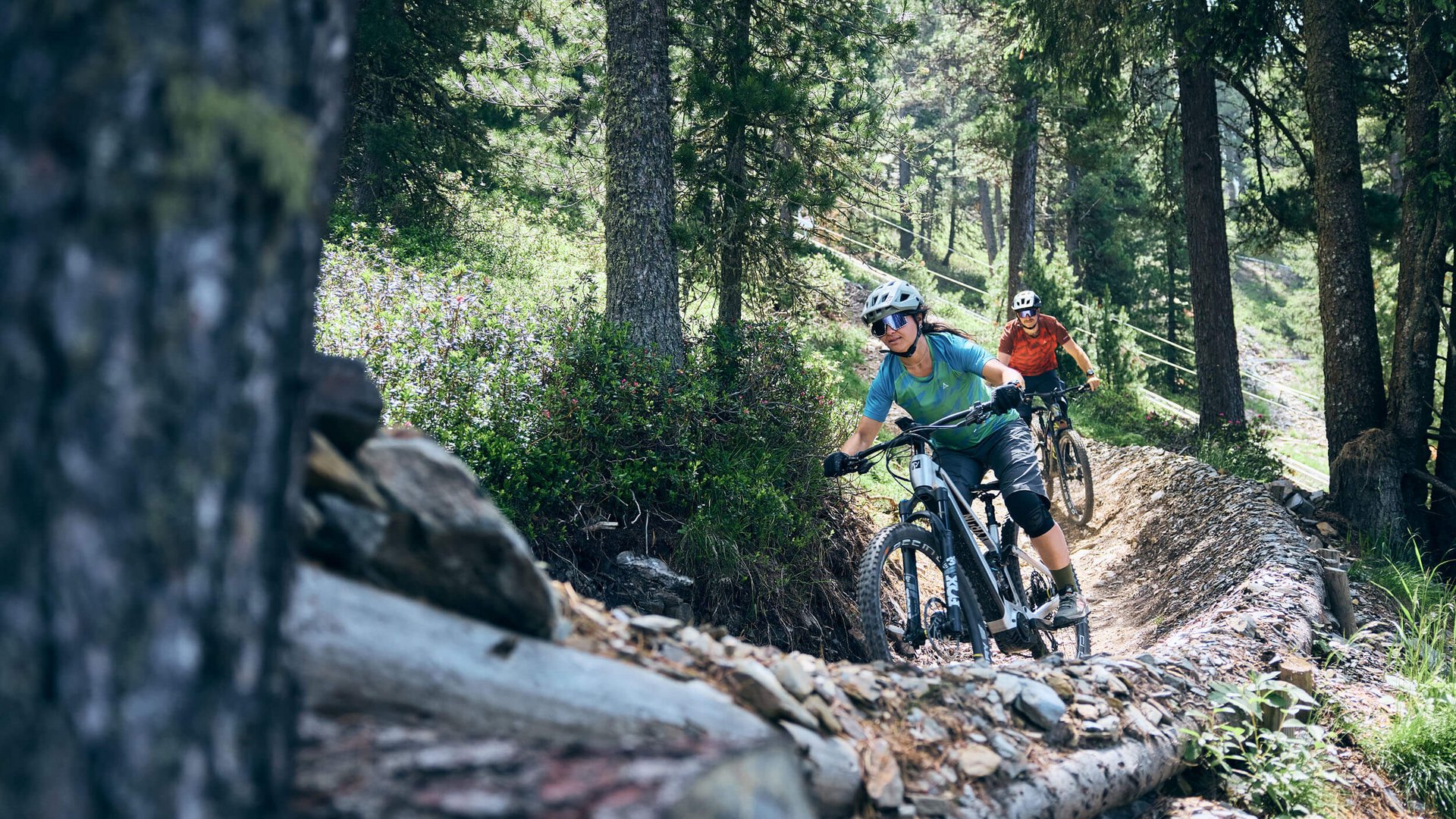 Zwei Mountainbiker fahren in einem bewaldeten Gebiet einen schmalen Pfad entlang (© Tobias Köhler)