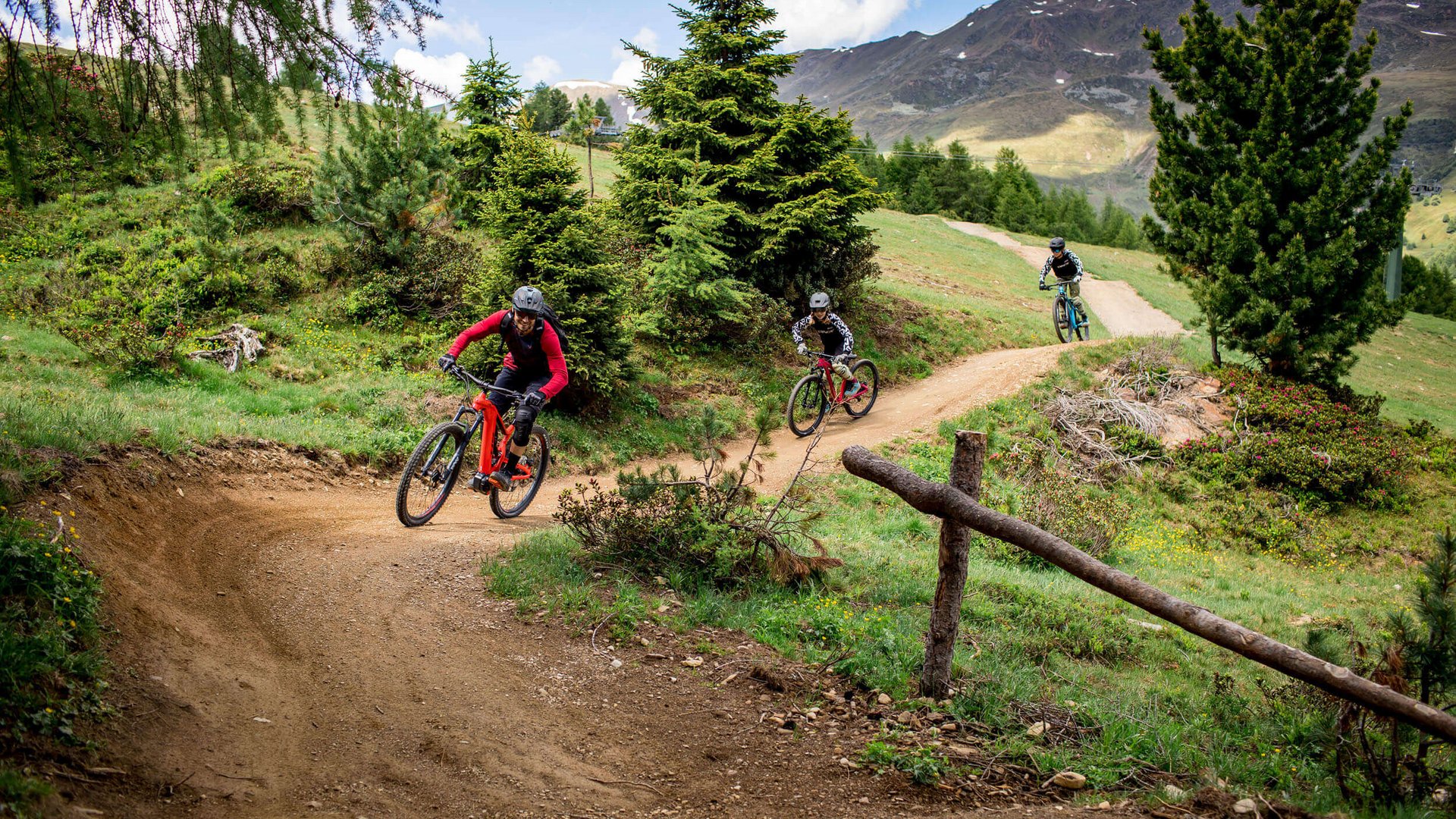 Drei Mountainbiker fahren auf einem kurvigen Bergweg durch grüne Landschaft (© Anne Kaiser Photography)