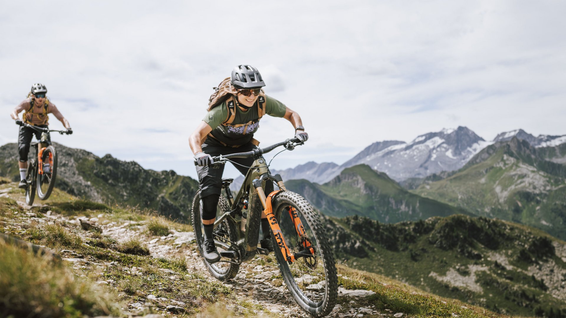 Zwei Mountainbiker fahren auf einem Bergweg mit Alpen im Hintergrund (© Martina Wunderle - Flo Distl)